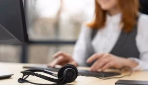 Auriculares de atención al cliente sobre un escritorio con una técnica trabajando al fondo.